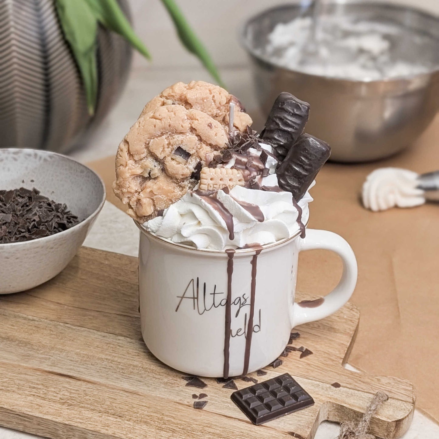 Zeigt eine Dessertkerze mit Wachs-Sahne und Schokotopping in einer weißen Tasse mit der Aufschrift "Alltagsheld", schräg von oben.