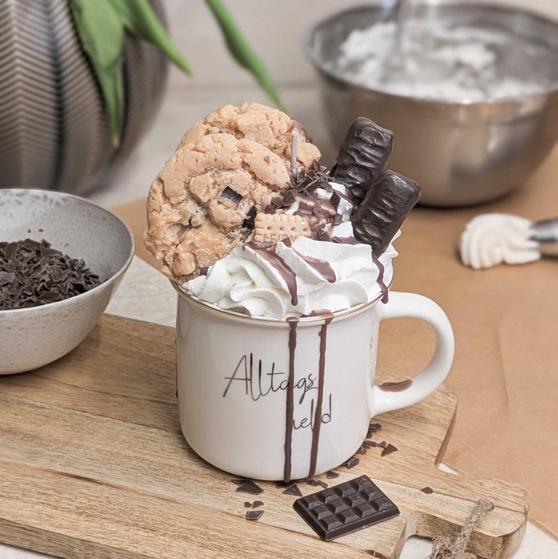 Zeigt eine Dessertkerze mit Wachs-Sahne und Schokotopping in einer weißen Tasse mit der Aufschrift "Alltagsheld", schräg von oben.